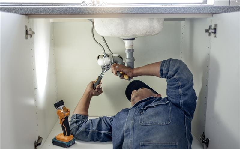 Plumber repairing pipes beneath a bathroom sink in West Covina